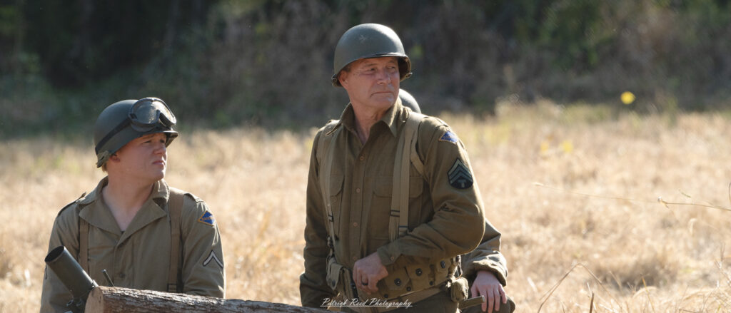 "U.S. Army officer in the field during World War II, standing confidently with a determined expression. Clad in a military uniform, the officer is surveying the surroundings, possibly planning the next strategic move. His cap is slightly tilted, and he carries a map or a communication device, embodying leadership and tactical awareness. The backdrop features a war-torn landscape, highlighting the challenges faced by military leaders during this historic conflict. This image captures the essence of duty and resolve among American officers in the field."